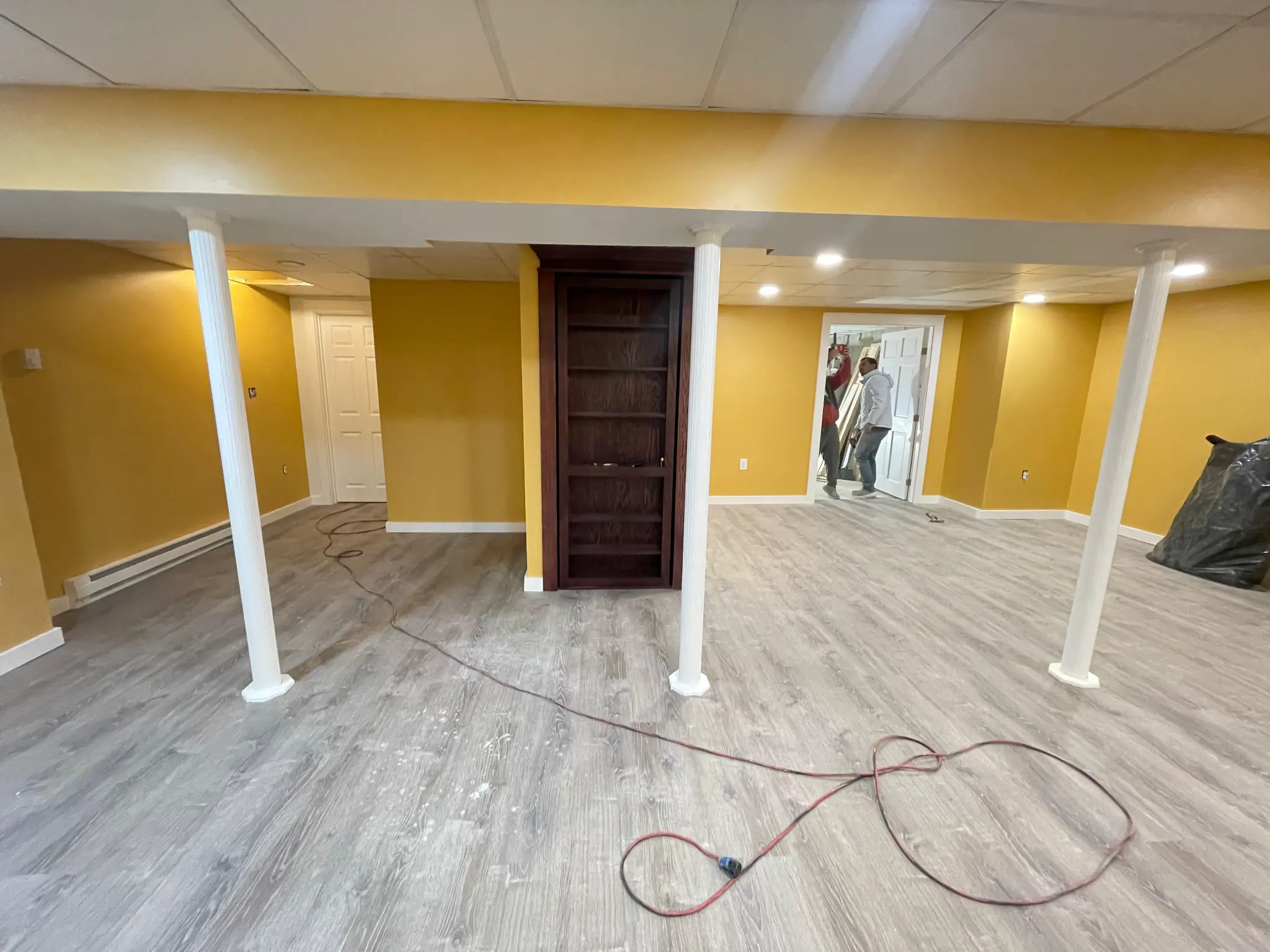 Finished basement with yellow walls gray LVP flooring and columns by Regulus Construction